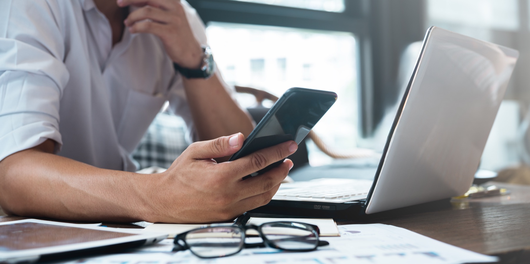 Persona haciendo cuentas con el celular y la computadora sobre el escritorio